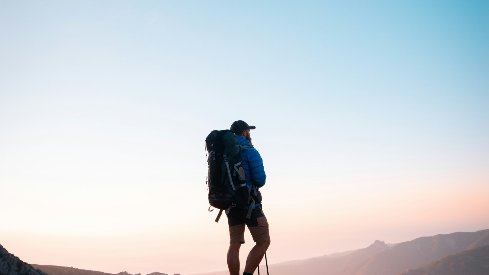 Backpacker with a large pack standing on a rocky peak at golden hour during a multi-day hike