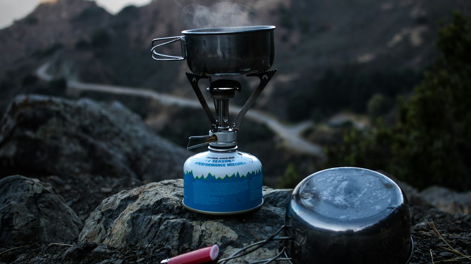 Backpacking gas stove and cooking pot on a cliff at sunset