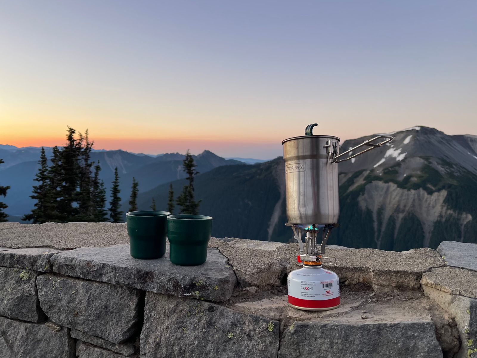 Camping stove and mugs on a stone wall in the mountains, ready for brewing coffee on a hike