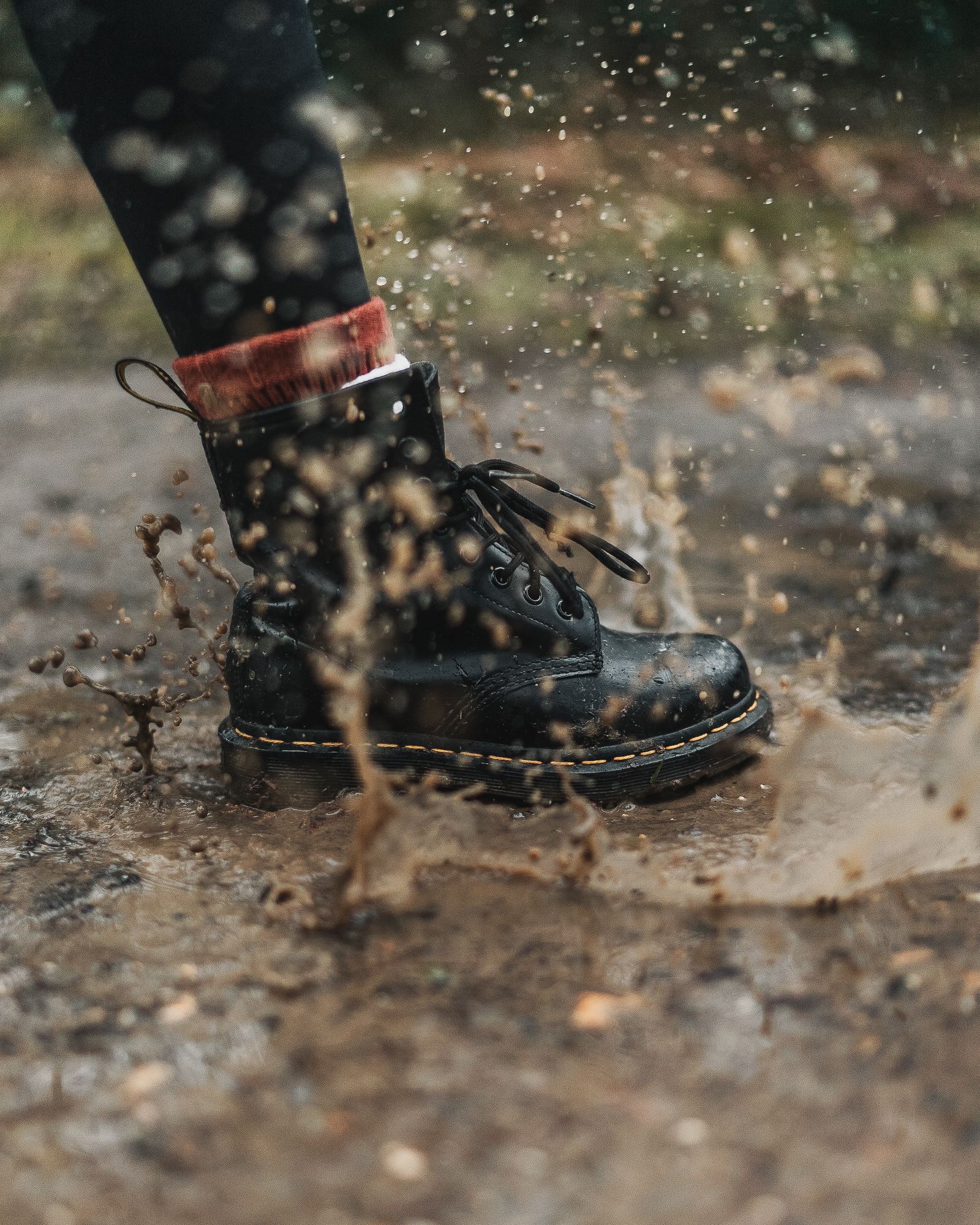 Boot splashing through a muddy puddle, showing why waterproof shoe covers and gaiters help on wet hikes