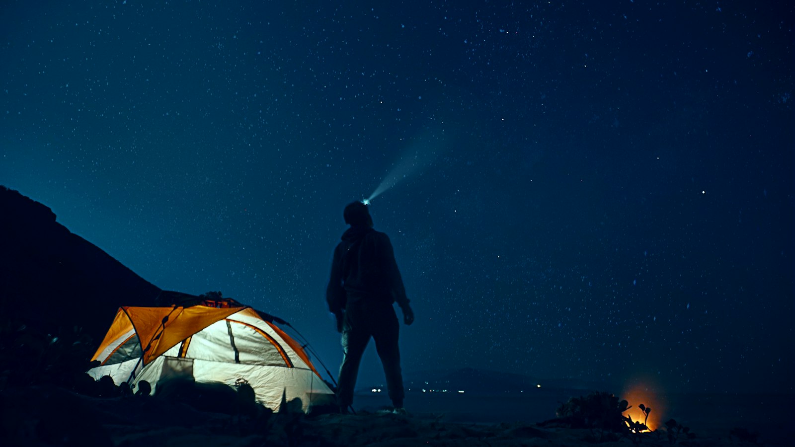 Camper wearing a headlamp standing beside a tent at night