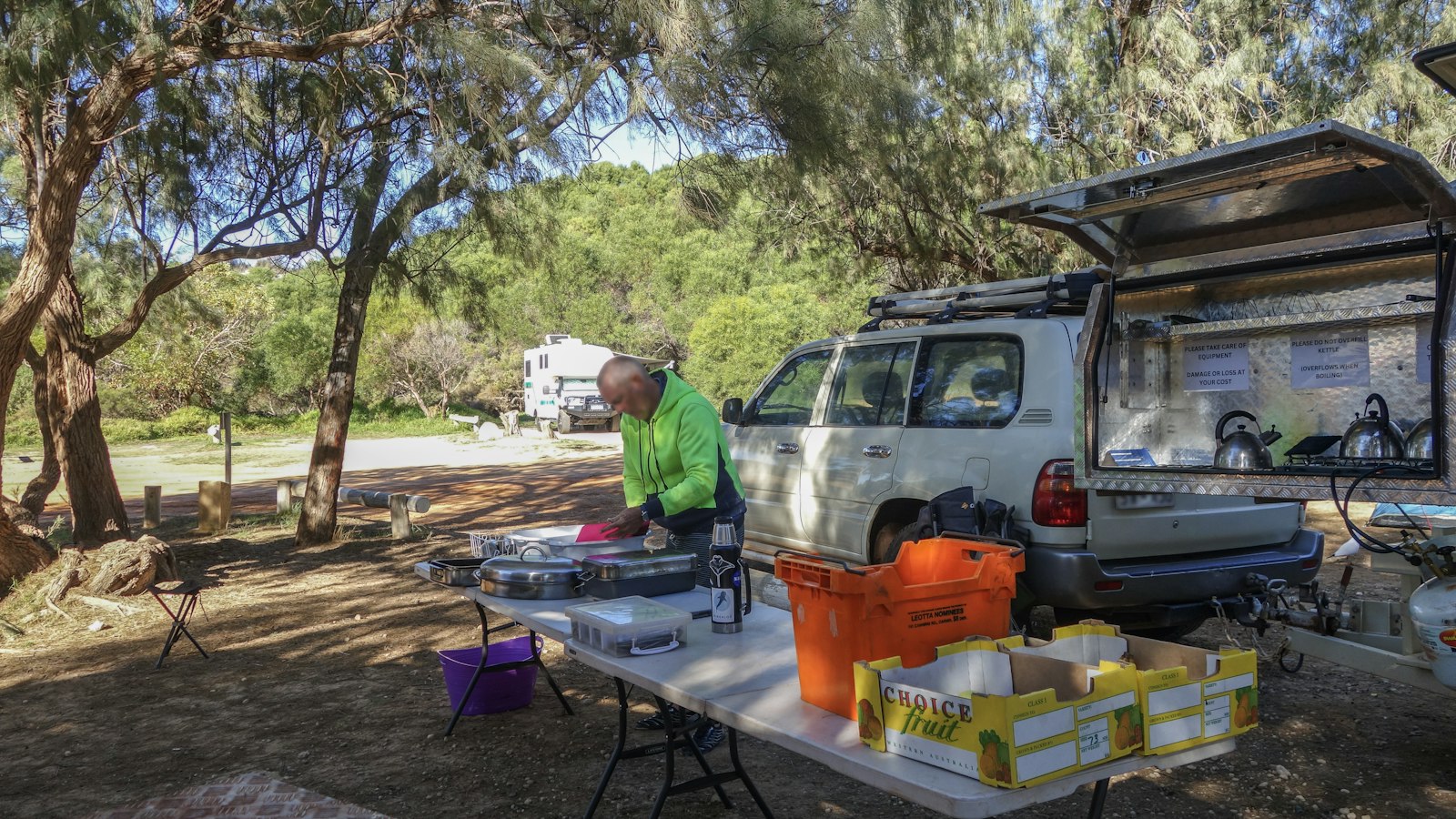 Man preparing items at an outdoor camp table beside a vehicle at a campsite