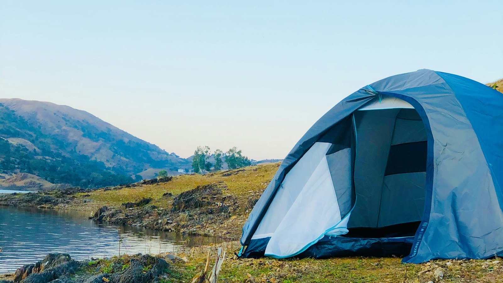 White dome tent on green grass near a body of water
