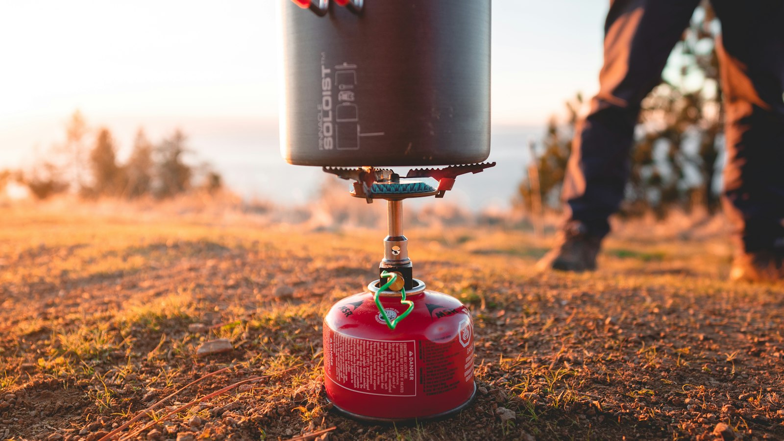 Gas canister stove and black cooking pot at sunset by the sea
