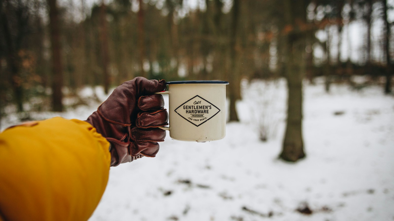 Hiker in gloves holding a warm camping mug in cold weather in the woods