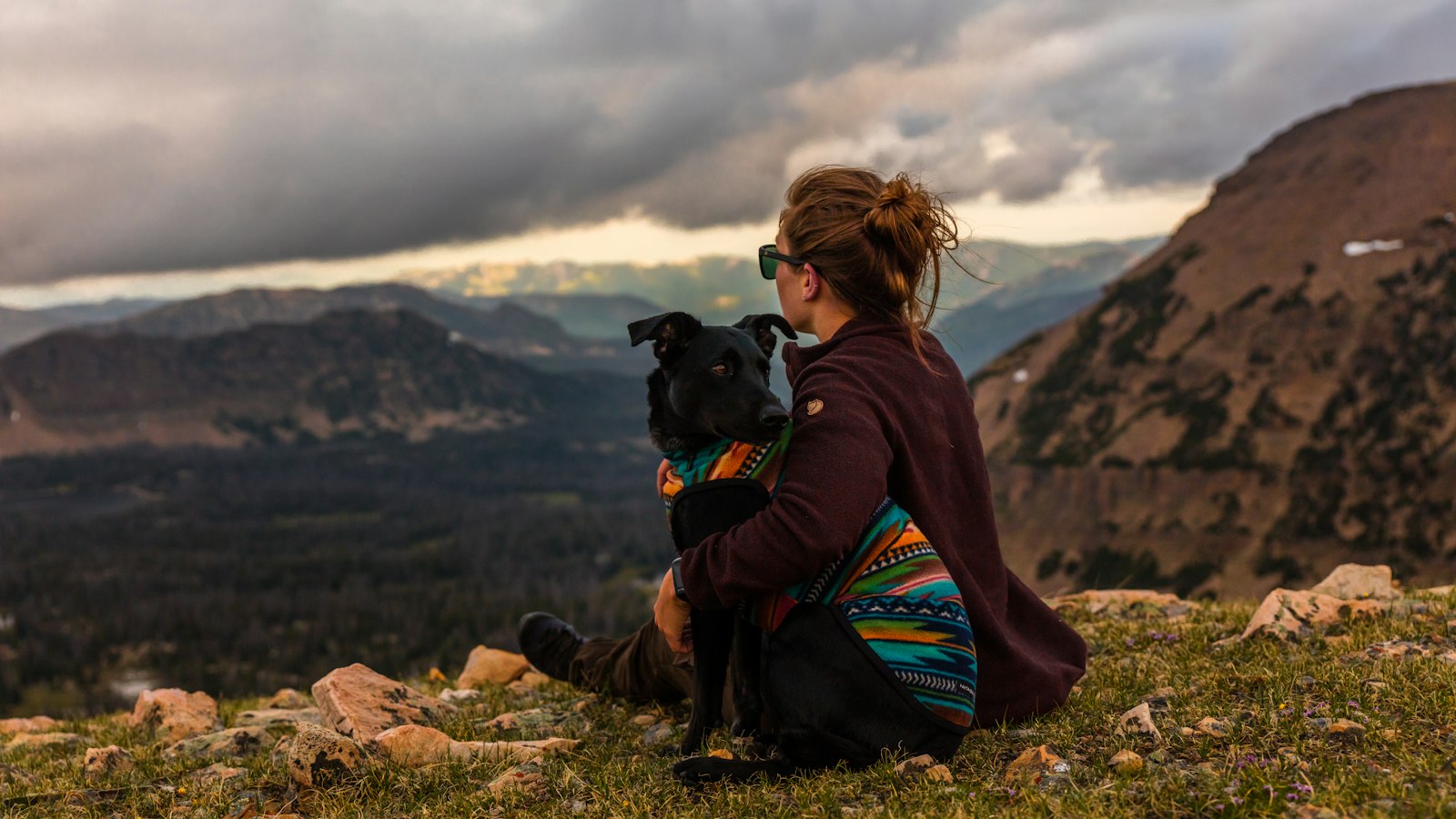 Hiker resting beside a black dog on a mountain top