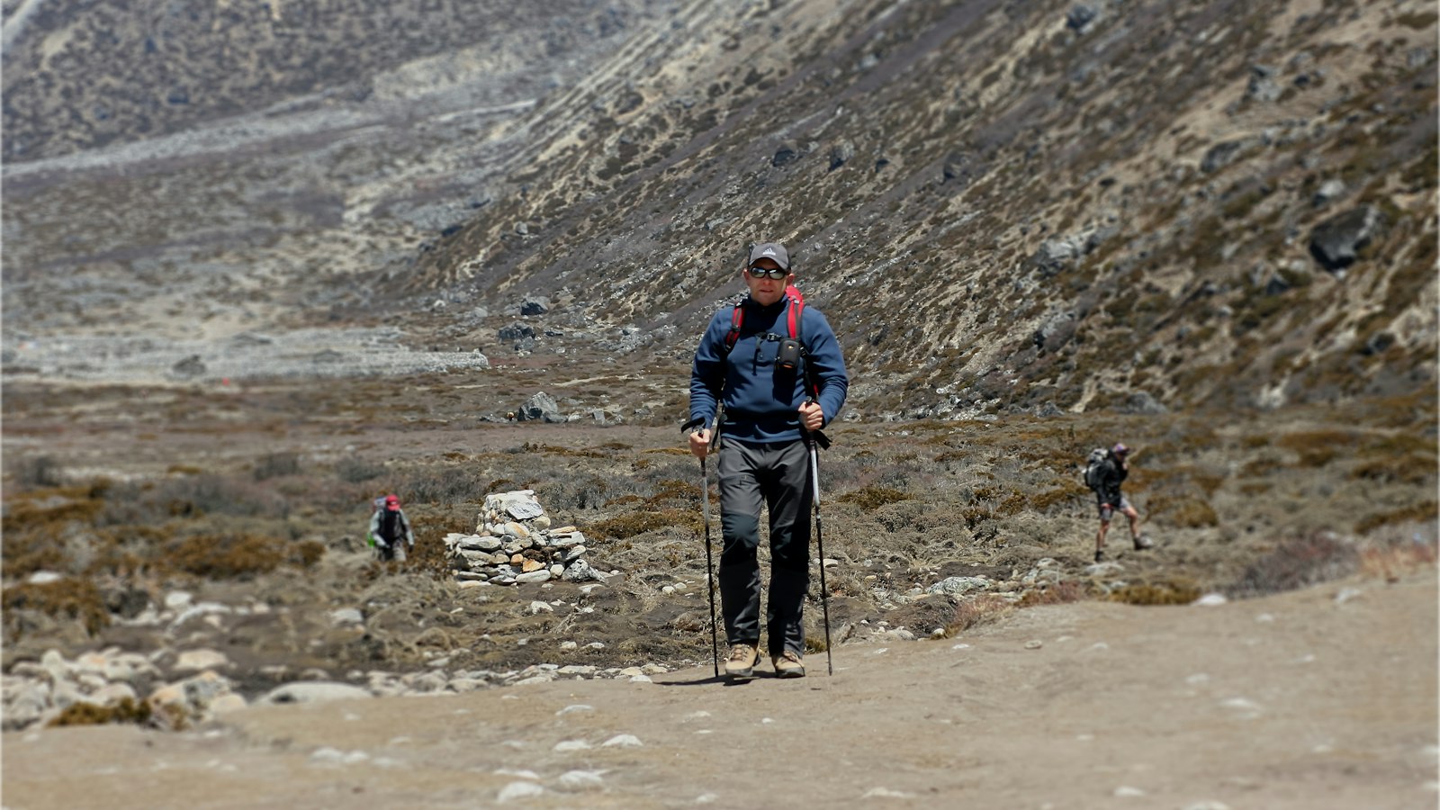 Hiker using trekking poles on a rocky trail in a mountain valley