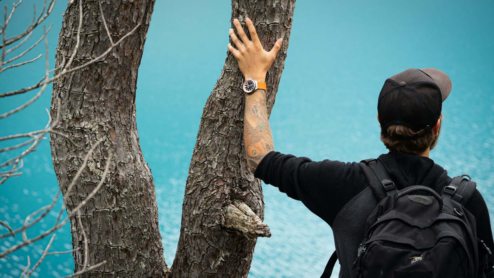 Hiker with a watch reaching up to a tree branch in the forest