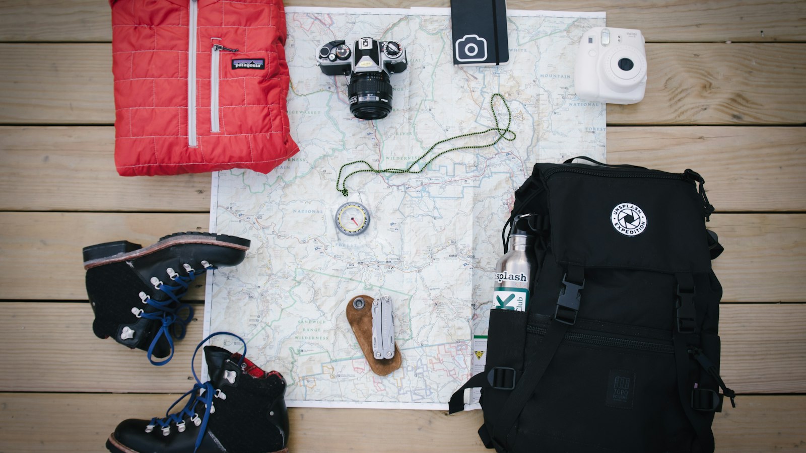 Hiking gear laid out on a map, including a backpack, boots, camera and jacket