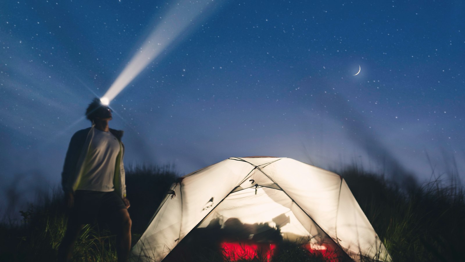Man with a bright headlamp in front of a camping tent