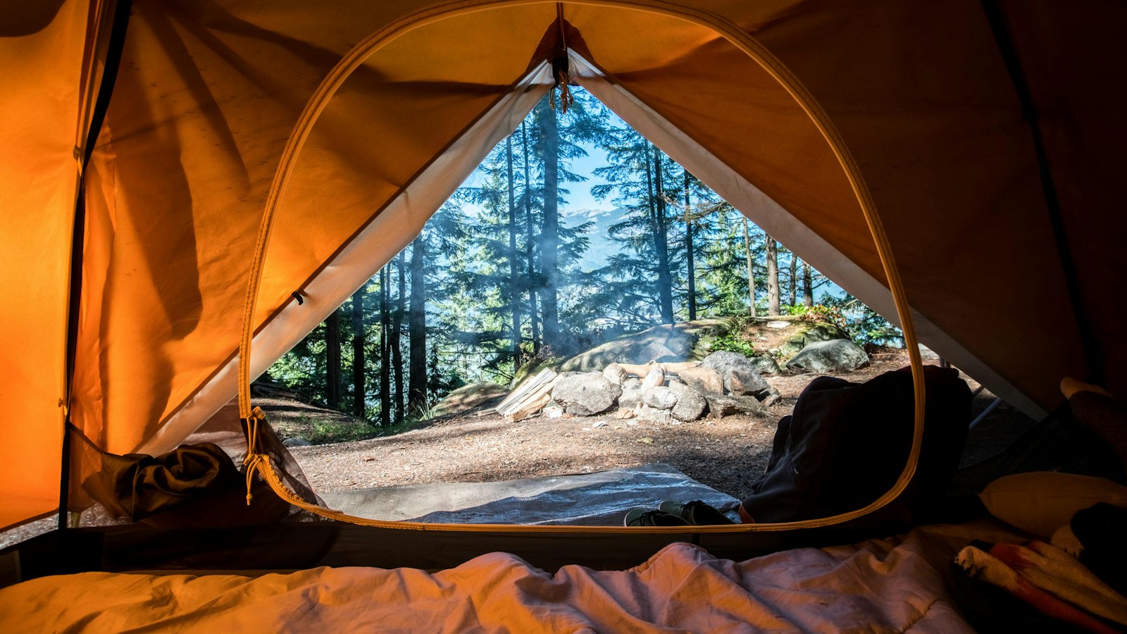 Orange camping tent pitched near green trees on a backpacking trip