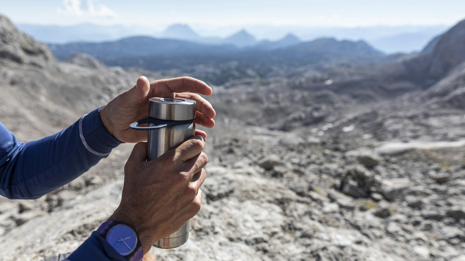 Solo hiker holding a metal cup on a forest hiking trail