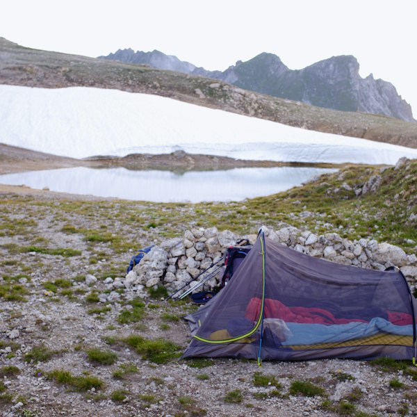 Backpacking tent beside a mountain lake with snow-covered peaks
