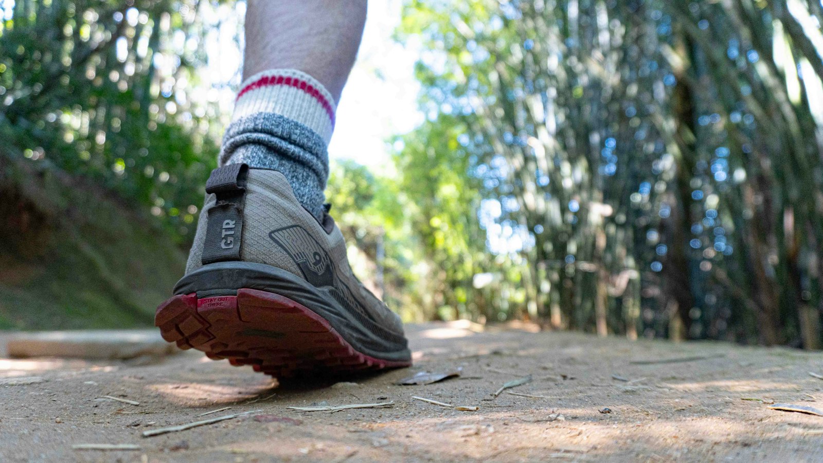 Trail running shoe and wool sock on a dusty dirt hiking path