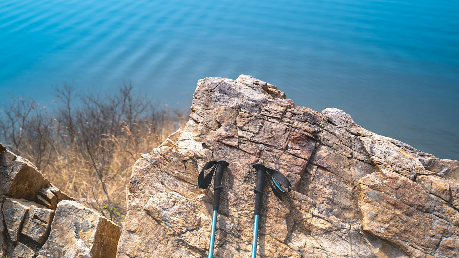 Pair of trekking poles resting on a rock overlooking a calm lake