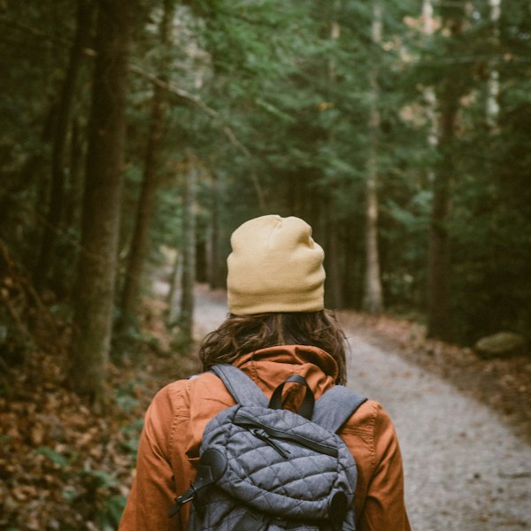 Woman hiker carrying a backpack toward a forest trail